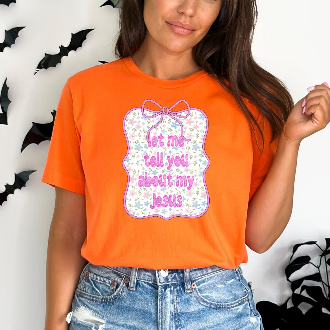 A woman wearing an orange t-shirt with a floral design and text, standing in front of a wall with bats.