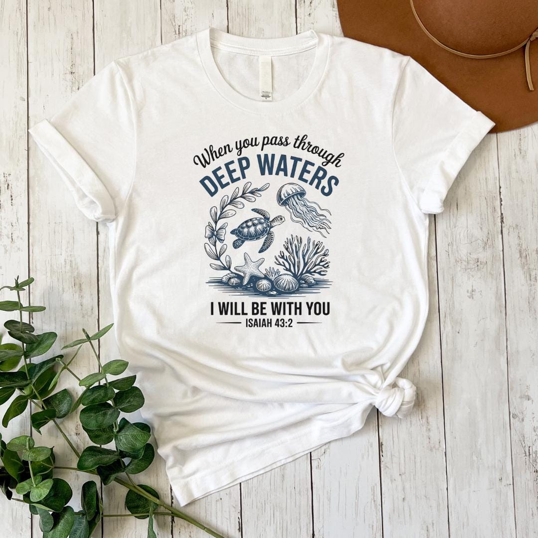 A white t-shirt with a graphic design featuring a turtle, jellyfish, and seaweed, along with the text "When you pass through DEEP WATERS, I WILL BE WITH YOU ISAIAH 43:2".