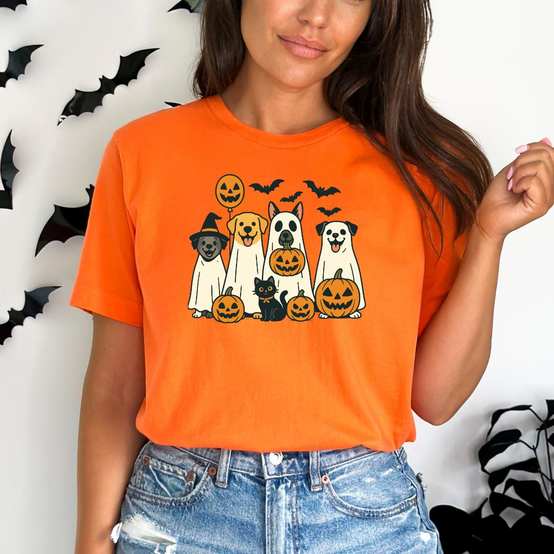 A woman wearing an orange t-shirt with a graphic of a group of dogs and cats, including a skeleton, a witch, and pumpkins, against a white background with black bats.