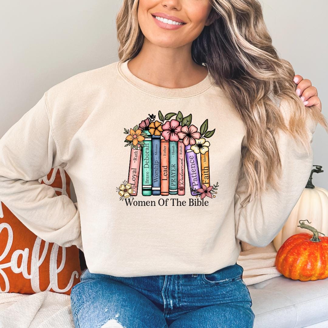 A woman wearing a white sweatshirt with a colorful graphic design of books and flowers, along with the text "Women Of The Bible".