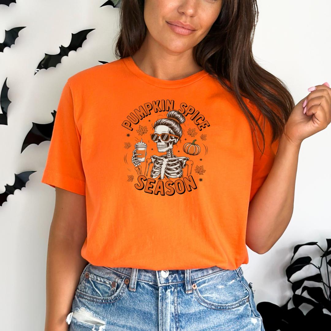 A woman wearing an orange t-shirt with a graphic design of a skeleton holding a cup and a pumpkin, along with the text "Pumpkin Spice Season".