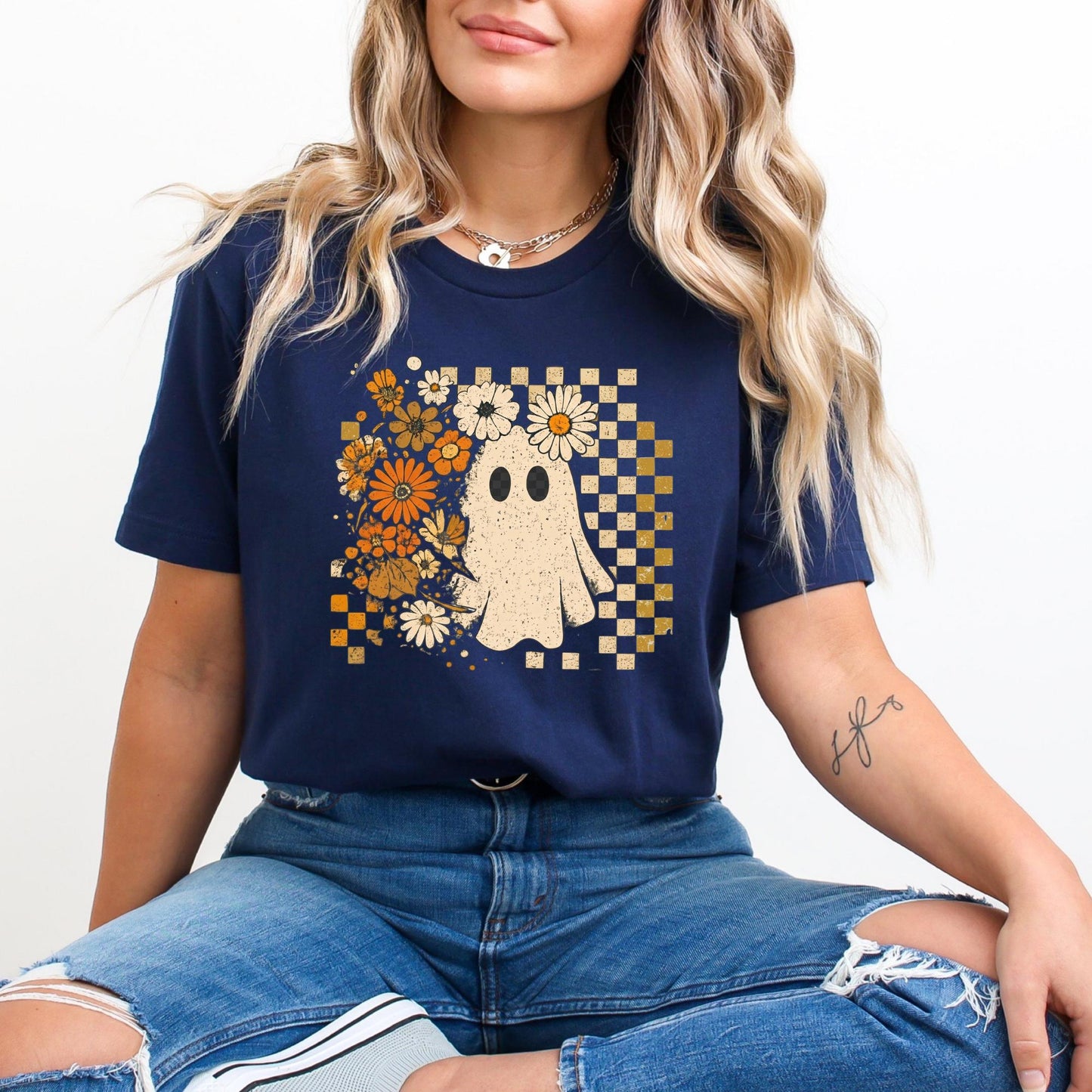 A woman wearing a navy blue t-shirt with a graphic of a ghost surrounded by flowers and a checkered pattern.