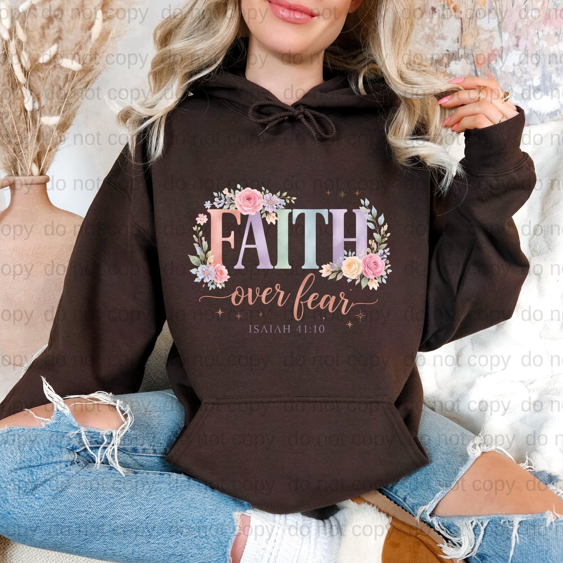 A woman wearing a brown hoodie with the text "FAITH over fear" printed on it, sitting on a couch.
