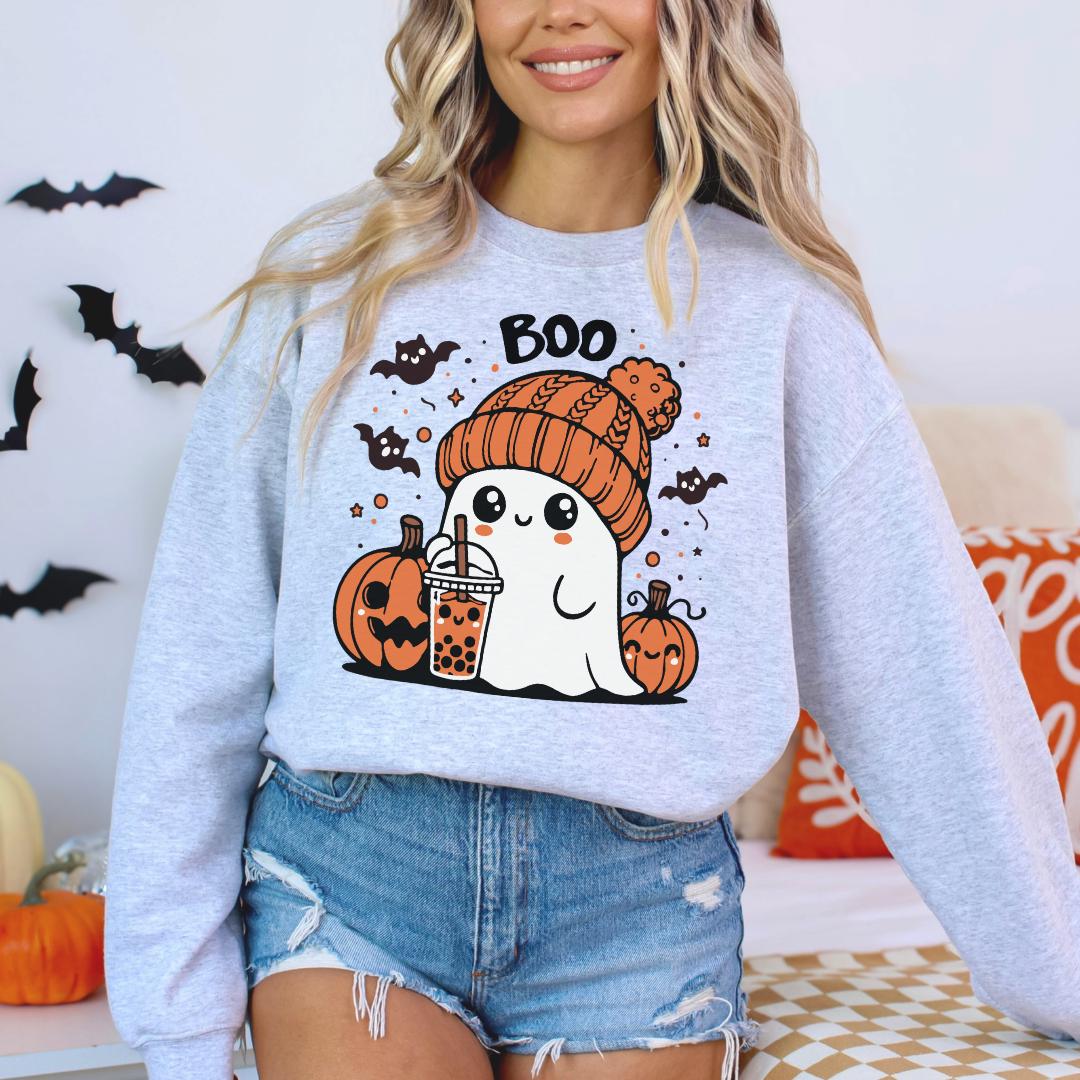 A woman wearing a grey sweatshirt with a graphic of a ghost holding a drink and surrounded by Halloween-themed elements.