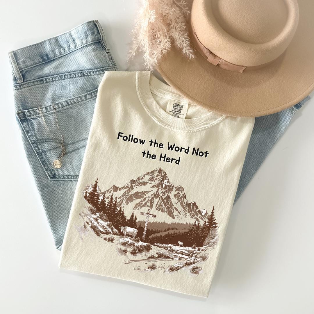 a white t-shirt with a mountain landscape design, a pair of blue jeans, and a beige hat.