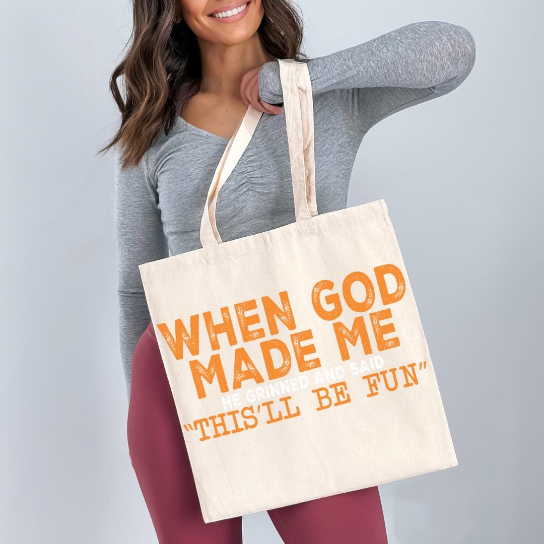 A woman holding a large tote bag with the text "WHEN GOD MADE ME" printed on it.