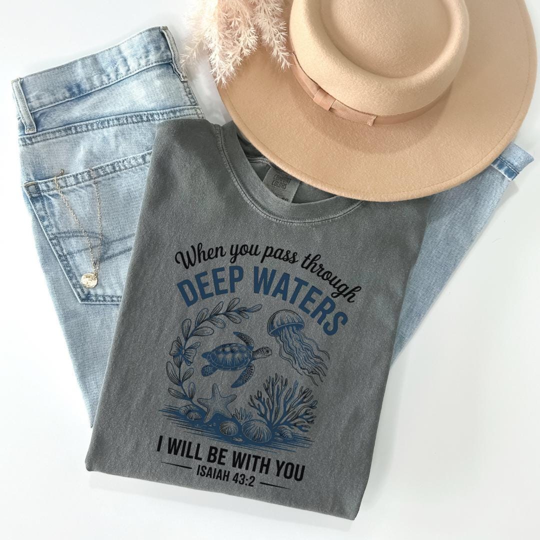 a gray t-shirt with a graphic design of marine life, including a turtle, jellyfish, and seaweed, along with the text "When you pass through DEEP WATERS I WILL BE WITH YOU" and the Bible verse " Isaiah 43:2".