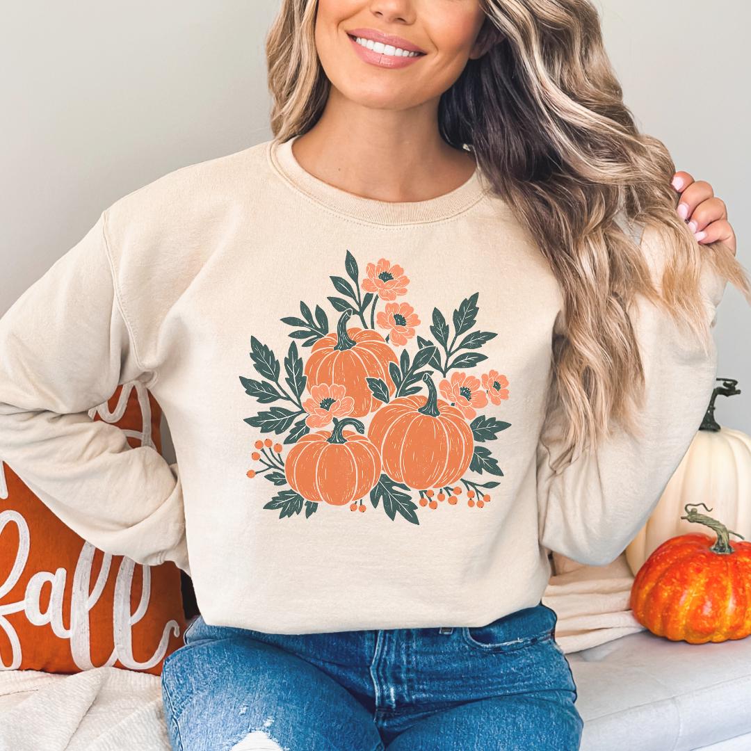 A woman wearing a beige sweater with a pumpkin and flower design, smiling and posing with her hand on her hip.