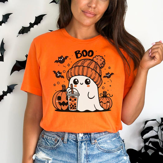 A woman wearing an orange t-shirt with a graphic of a ghost holding a drink and surrounded by bats and pumpkins.