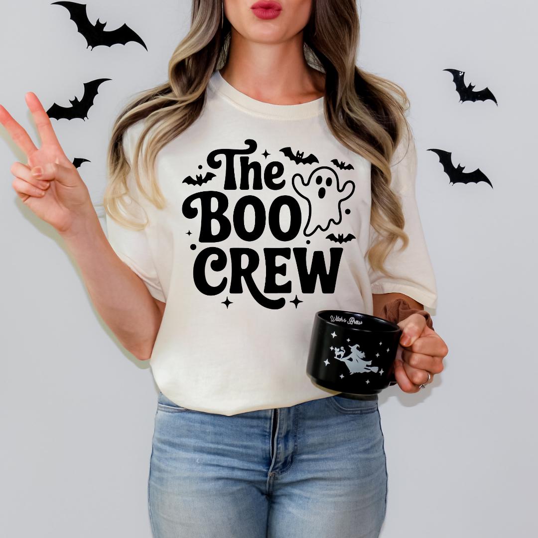 A woman wearing a white t-shirt with the text "The Boo Crew" and holding a black mug with a ghost design.