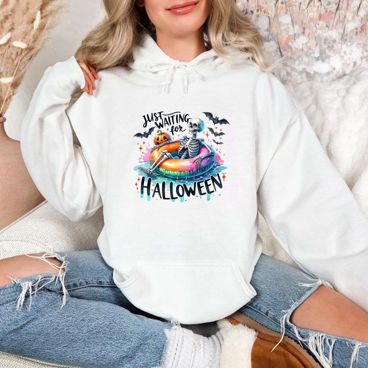 A woman wearing a white hoodie with a Halloween-themed graphic and text.