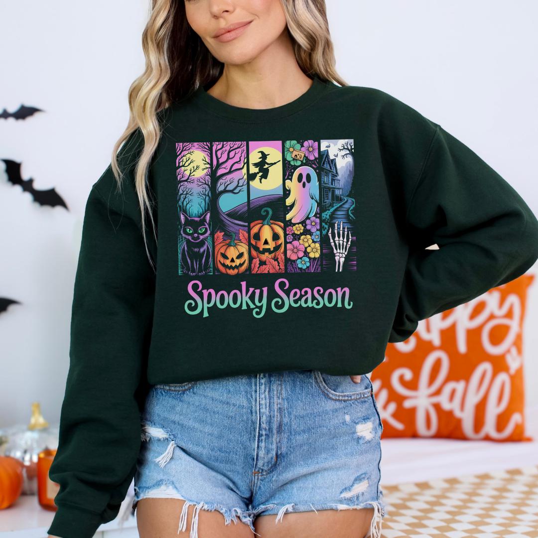 A woman wearing a black sweatshirt with a graphic design featuring Halloween-themed illustrations and the text "Spooky Season" printed on it.