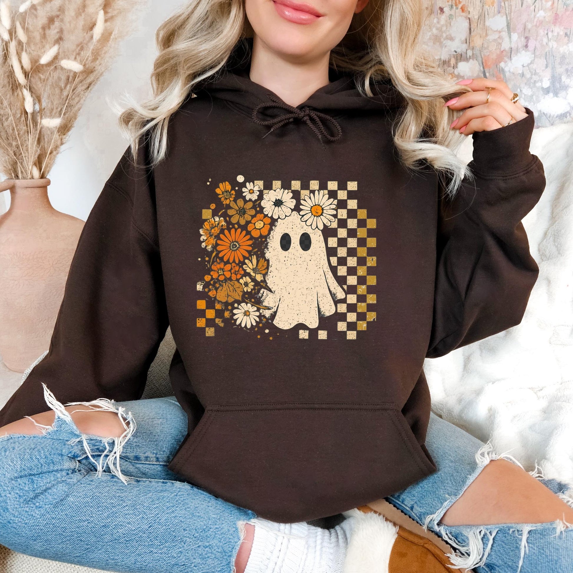 A woman wearing a brown hoodie with a graphic of a ghost surrounded by flowers and a checkered pattern.