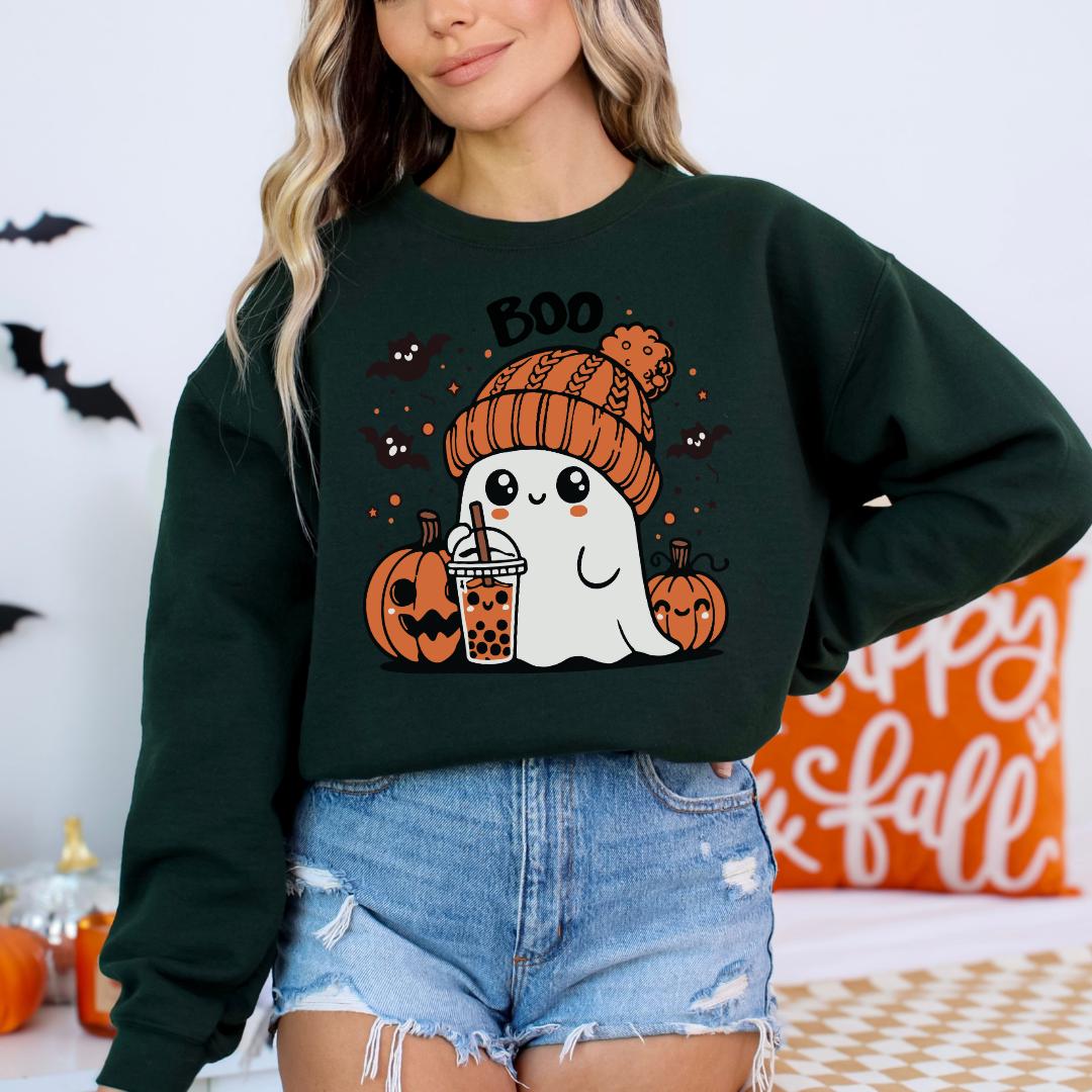 A woman wearing a green sweatshirt with a graphic of a ghost holding a drink and surrounded by pumpkins and bats.