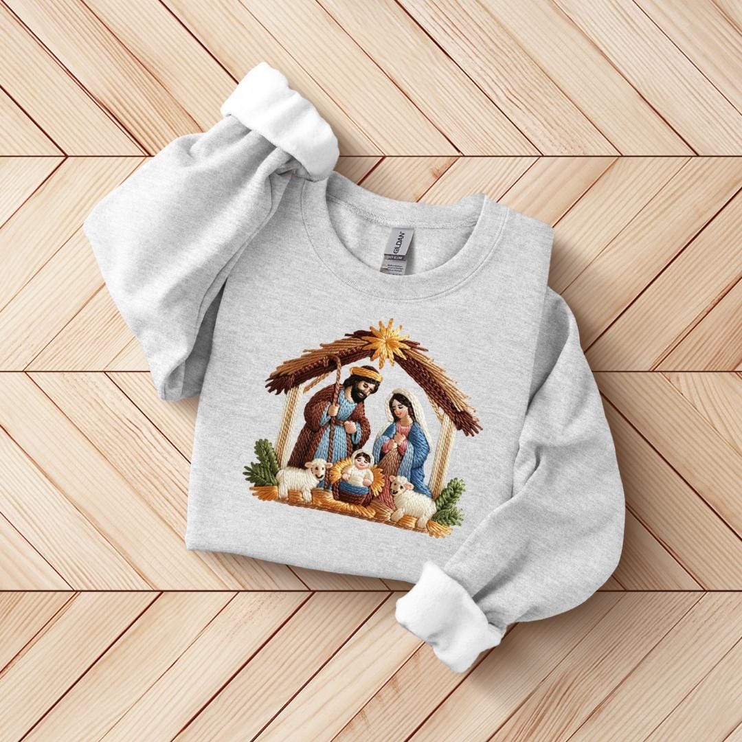 A gray sweatshirt with a nativity scene design printed on it, laid out on a wooden surface.