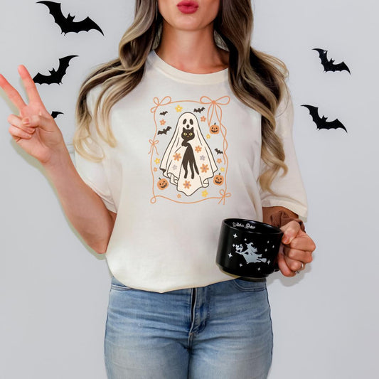 A woman wearing a white t-shirt with a Halloween-themed graphic and holding a black mug with a Halloween-themed design.