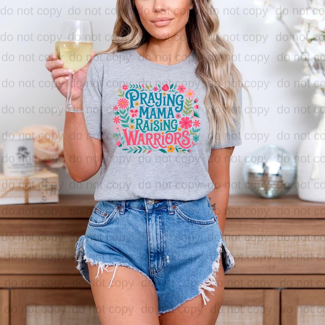 A woman wearing a gray t-shirt with a floral design and denim shorts is holding a glass of wine.