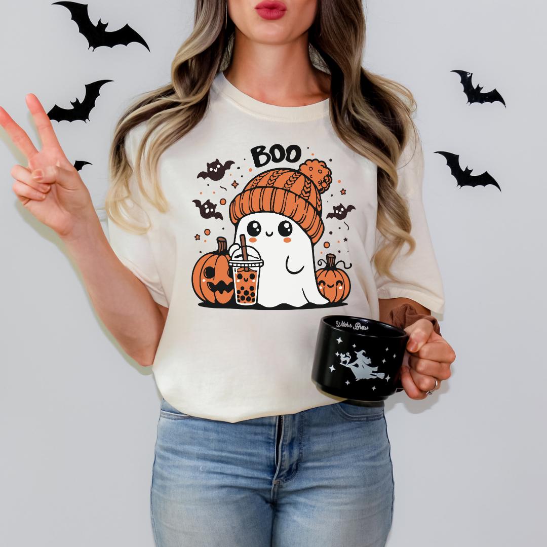 A woman wearing a white t-shirt with a cartoon ghost and Halloween-themed elements, holding a black mug with a design of a witch.