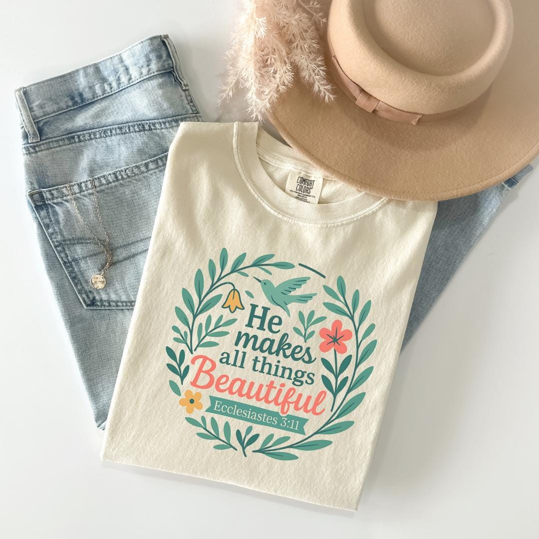 a white t-shirt with a colorful graphic design, a pair of blue jeans, and a beige hat, all laid out on a white surface.