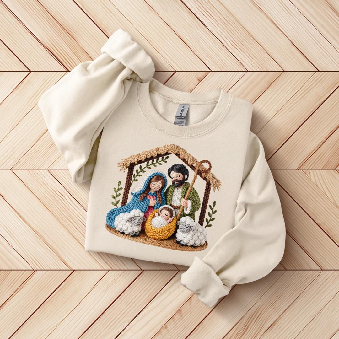 A white sweater with a detailed embroidered image of the Holy Family, including the Virgin Mary, baby Jesus, and baby Joseph, sitting in a nativity scene.