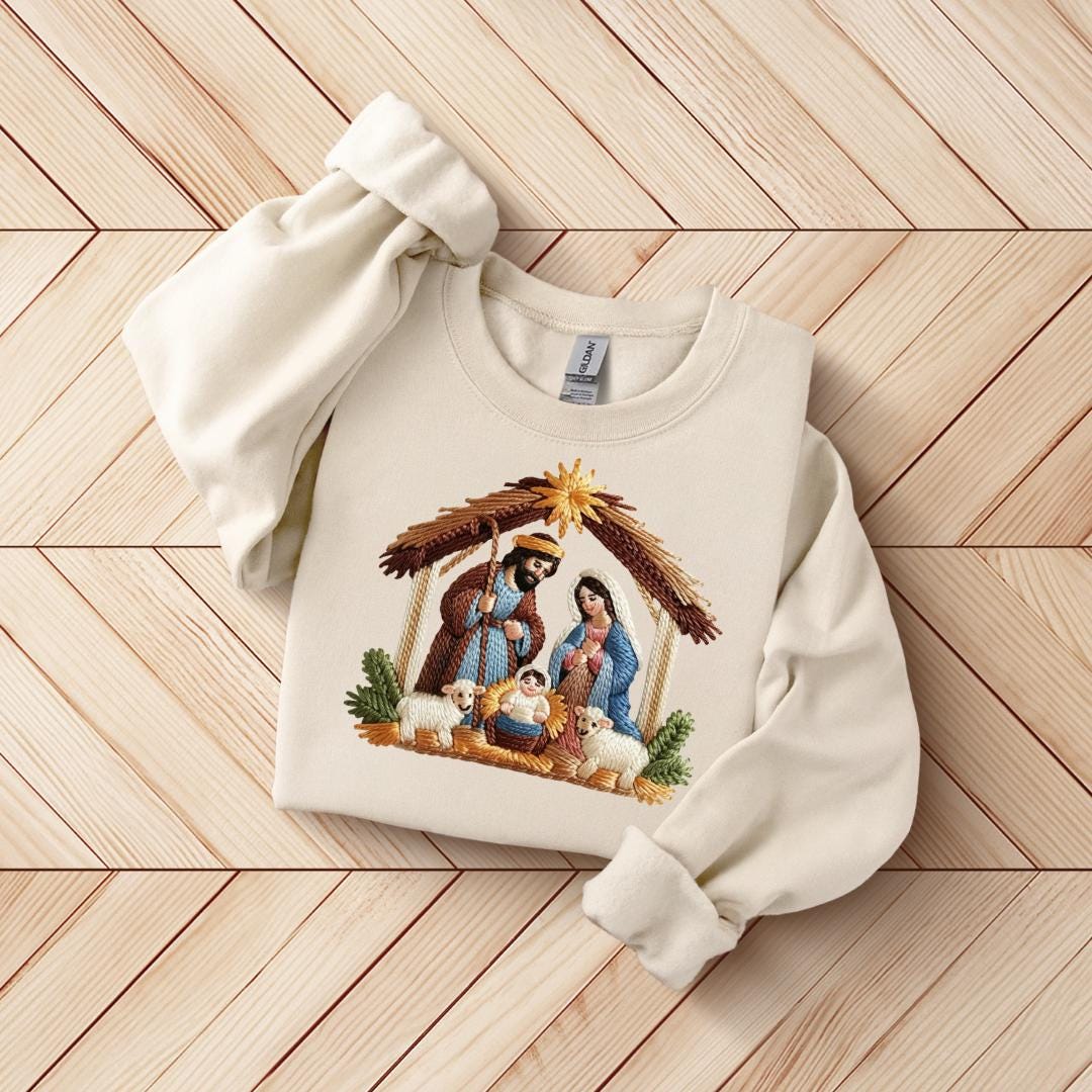 A white sweater with a detailed embroidered image of the nativity scene, featuring the figures of the Virgin Mary, baby Jesus, and the wise men.