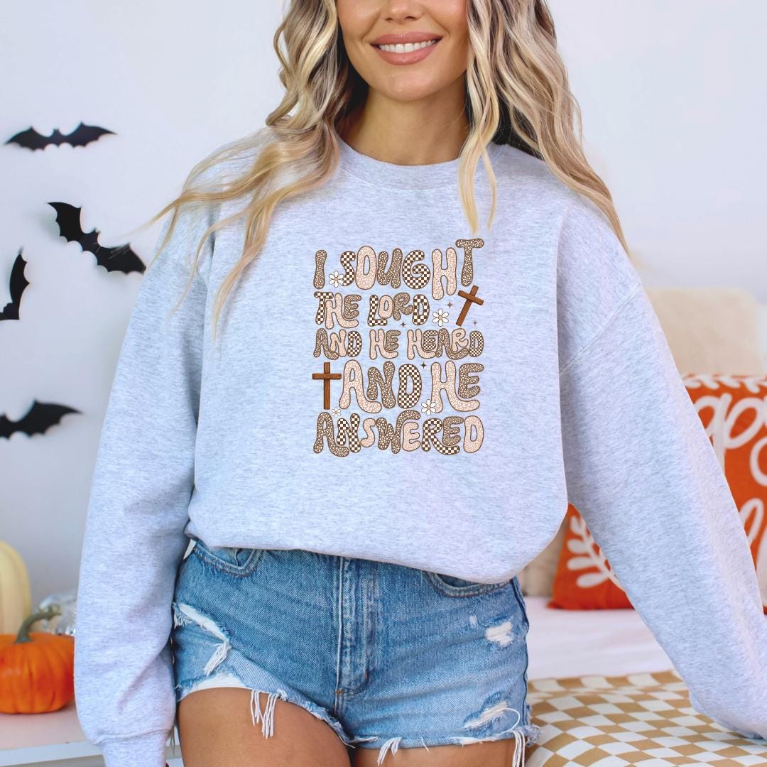 A woman wearing a gray sweatshirt with a printed design on it, standing in front of a Halloween-themed background.