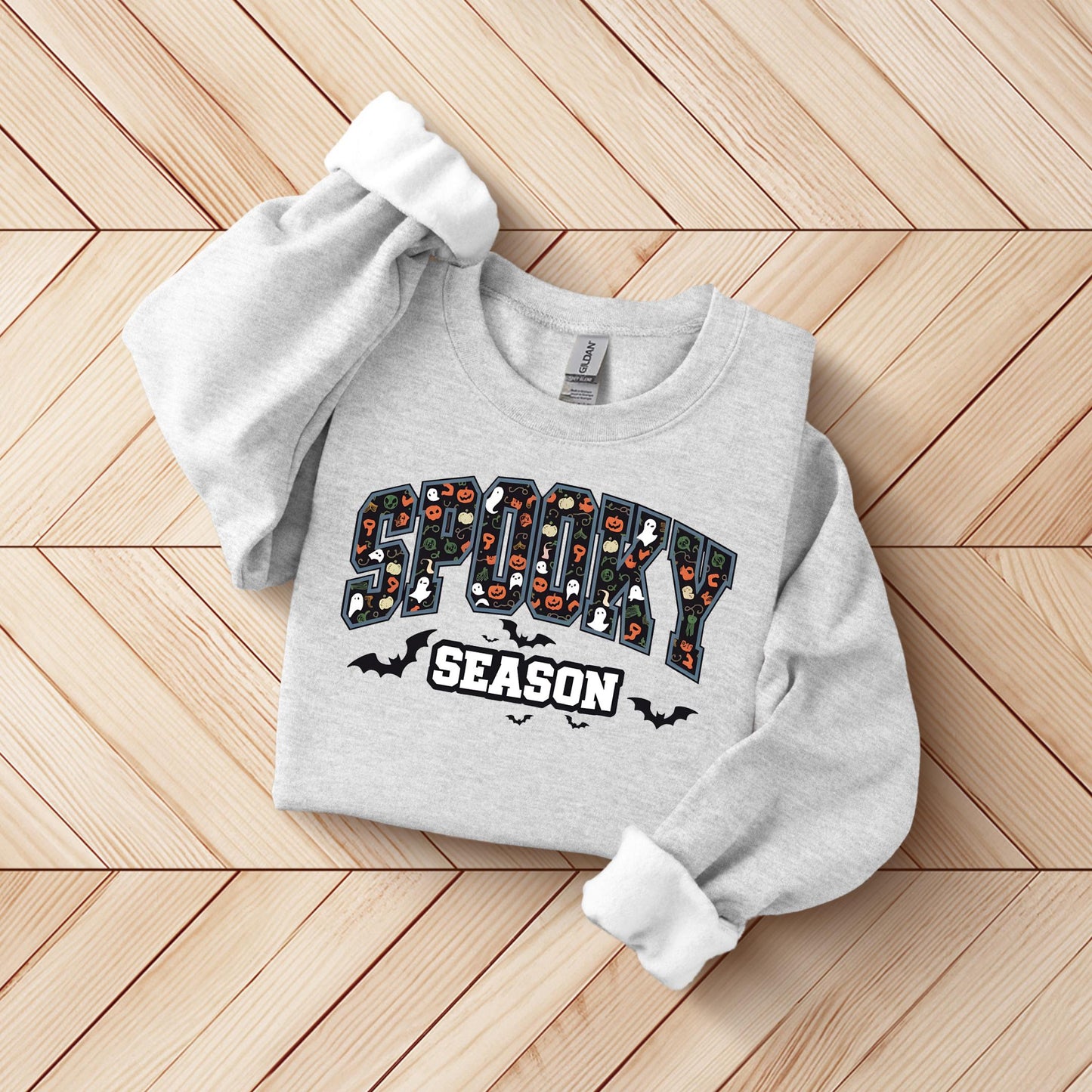 A gray sweatshirt with the text "SPOOKY SEASON" printed on it, along with various Halloween-themed graphics such as bats, skulls, and ghosts.