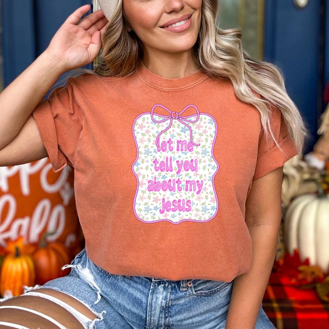 A woman wearing a red t-shirt with a floral design and text, smiling and posing in front of a background with pumpkins and a blue door.