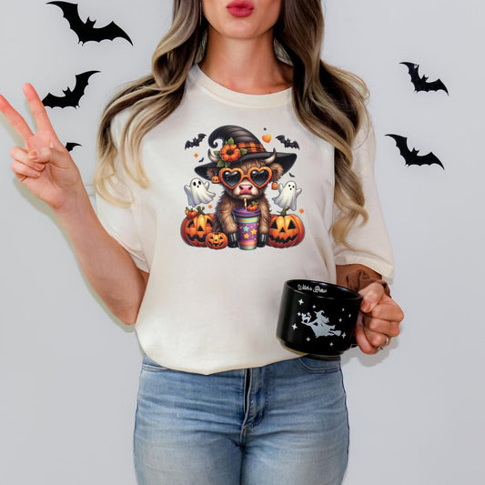 A woman wearing a white t-shirt with a Halloween-themed graphic of a cow, holding a black mug with a star design.