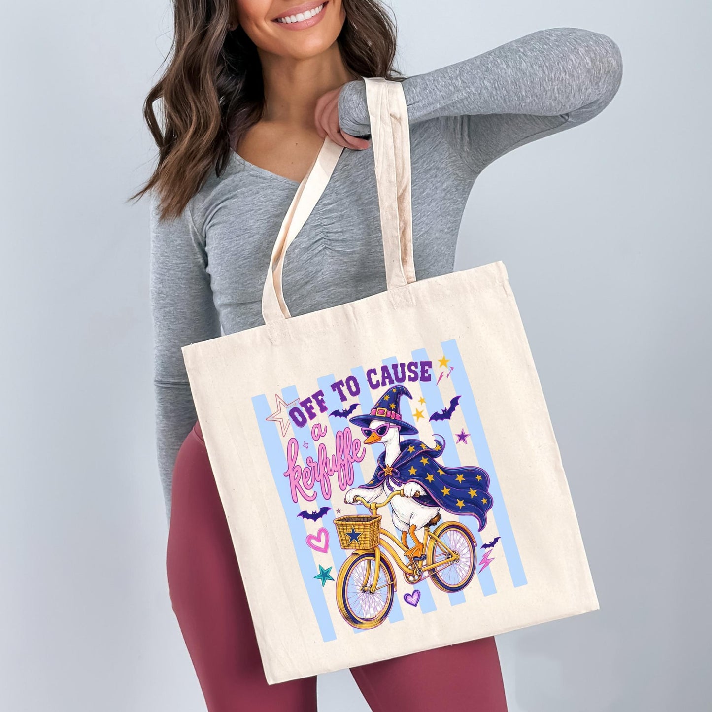 A woman is holding a large tote bag with a cartoon image of a bicycle and a witch on it.