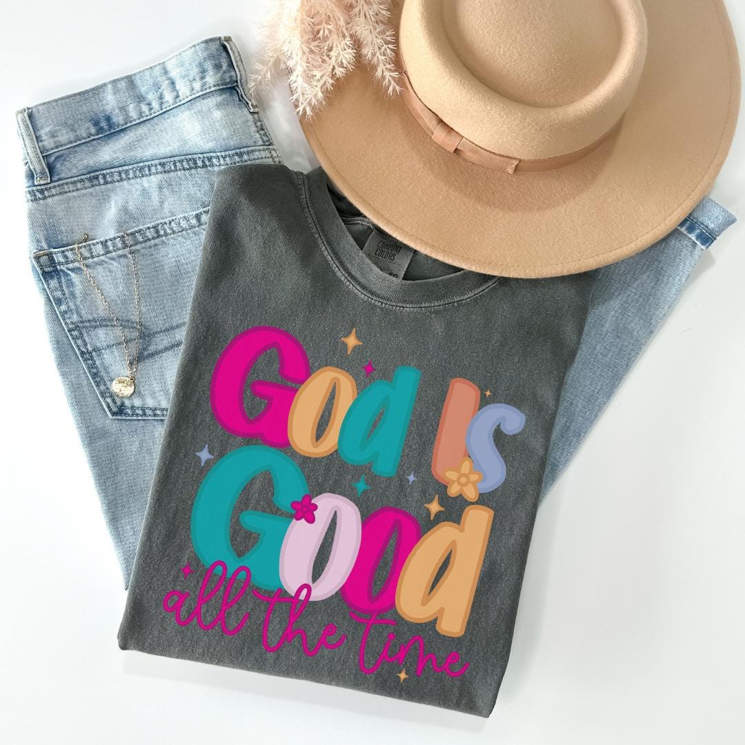 A gray t-shirt with colorful text, a pair of jeans, and a beige hat are arranged on a white background.