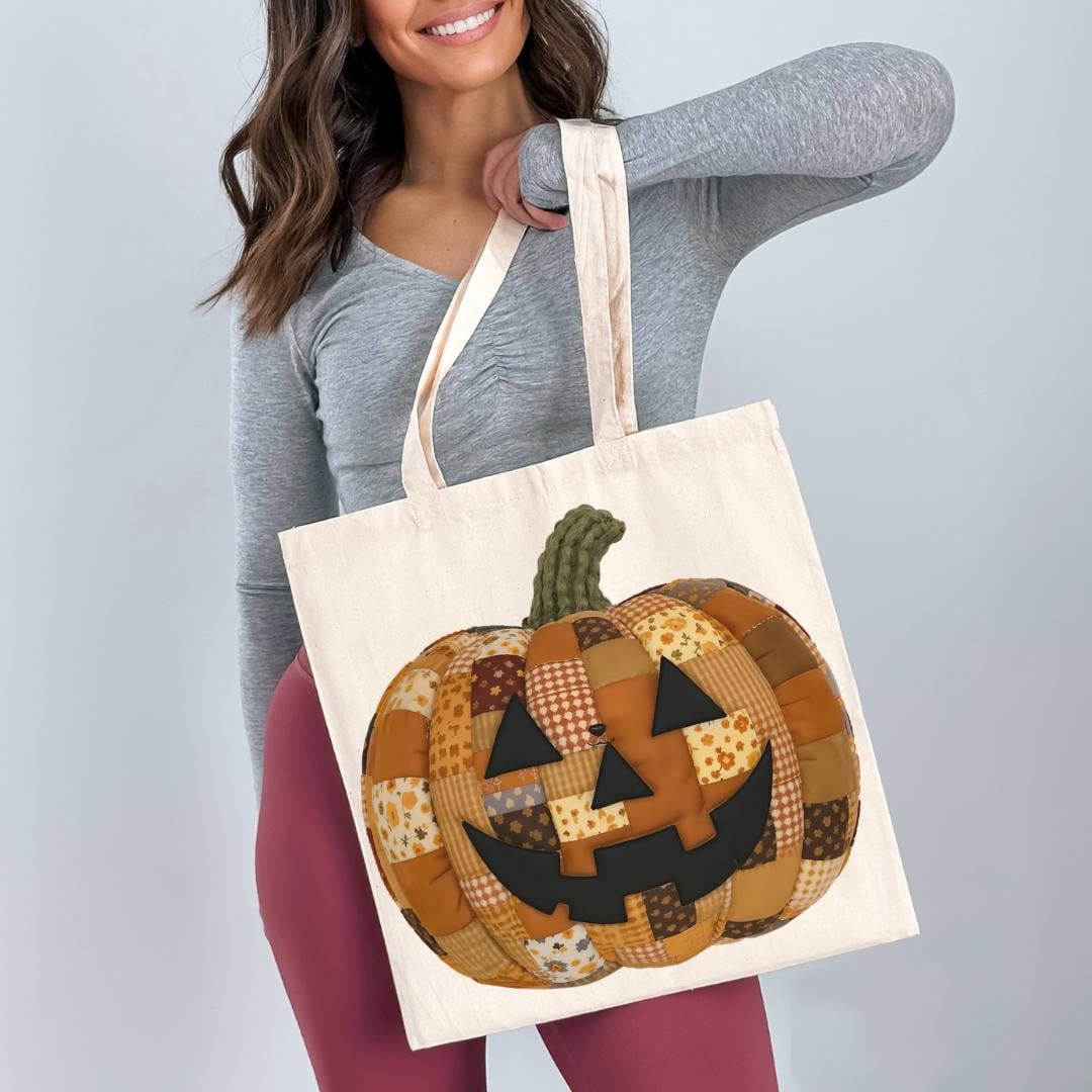 A woman is holding a white tote bag with a patchwork pumpkin design on it.
