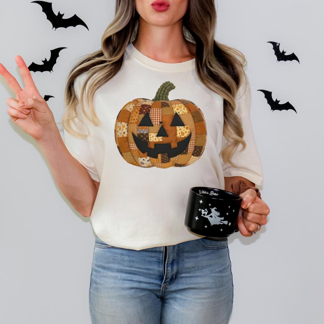 A woman is standing against a white background, wearing a white t-shirt with a pumpkin patch design and holding a black mug with a white star design.