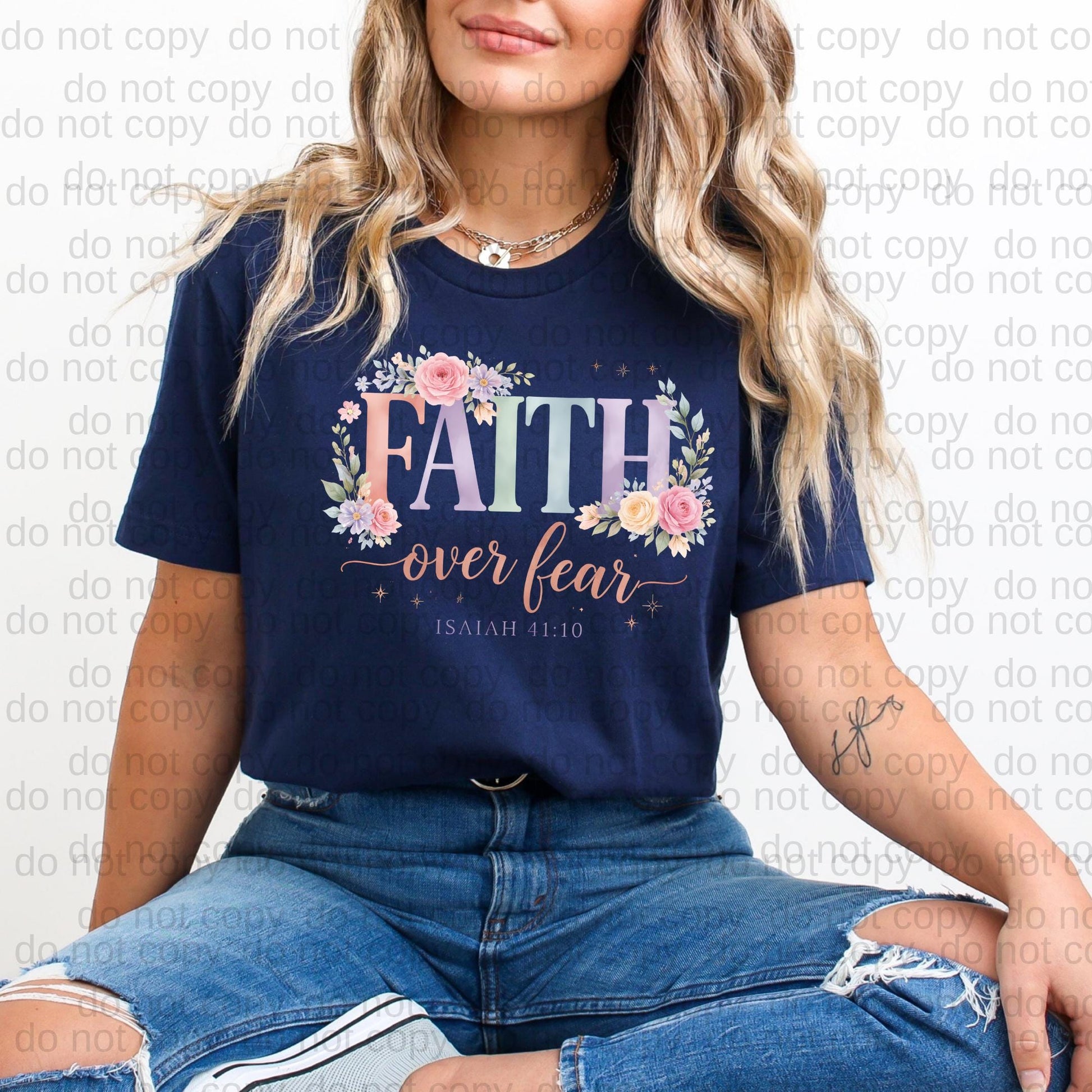 A woman wearing a navy blue t-shirt with the text "FAITH over fear" and floral designs, sitting on the ground with her legs crossed.