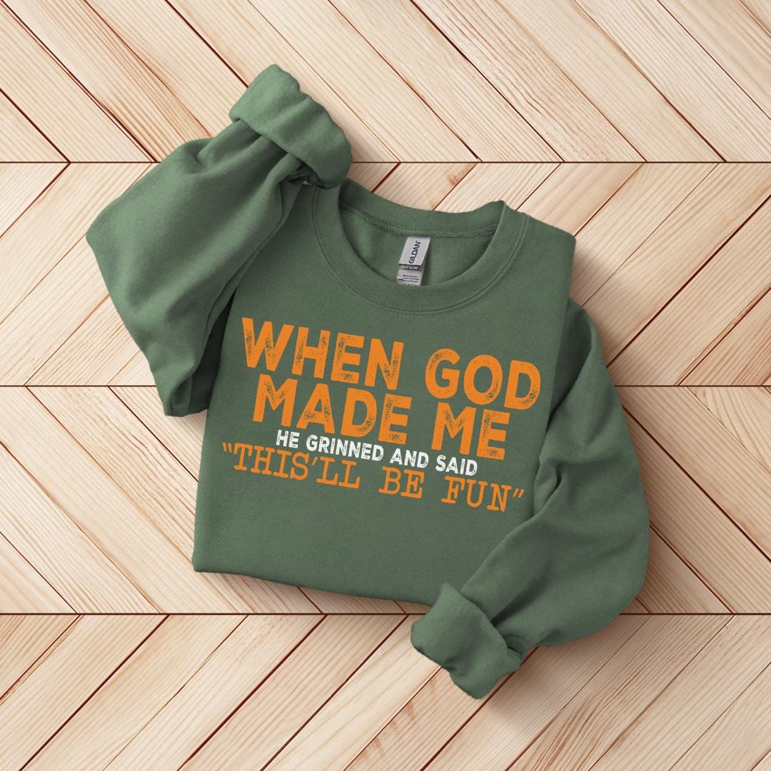 A green sweatshirt with orange text printed on it, laid out on a wooden surface.