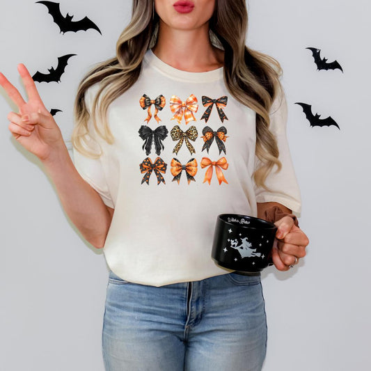 A woman is standing against a white background, wearing a white t-shirt with a graphic of bows and holding a black mug with a white design.