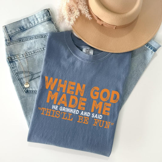 A blue t-shirt with orange text, a pair of jeans, and a beige hat are arranged on a white background.