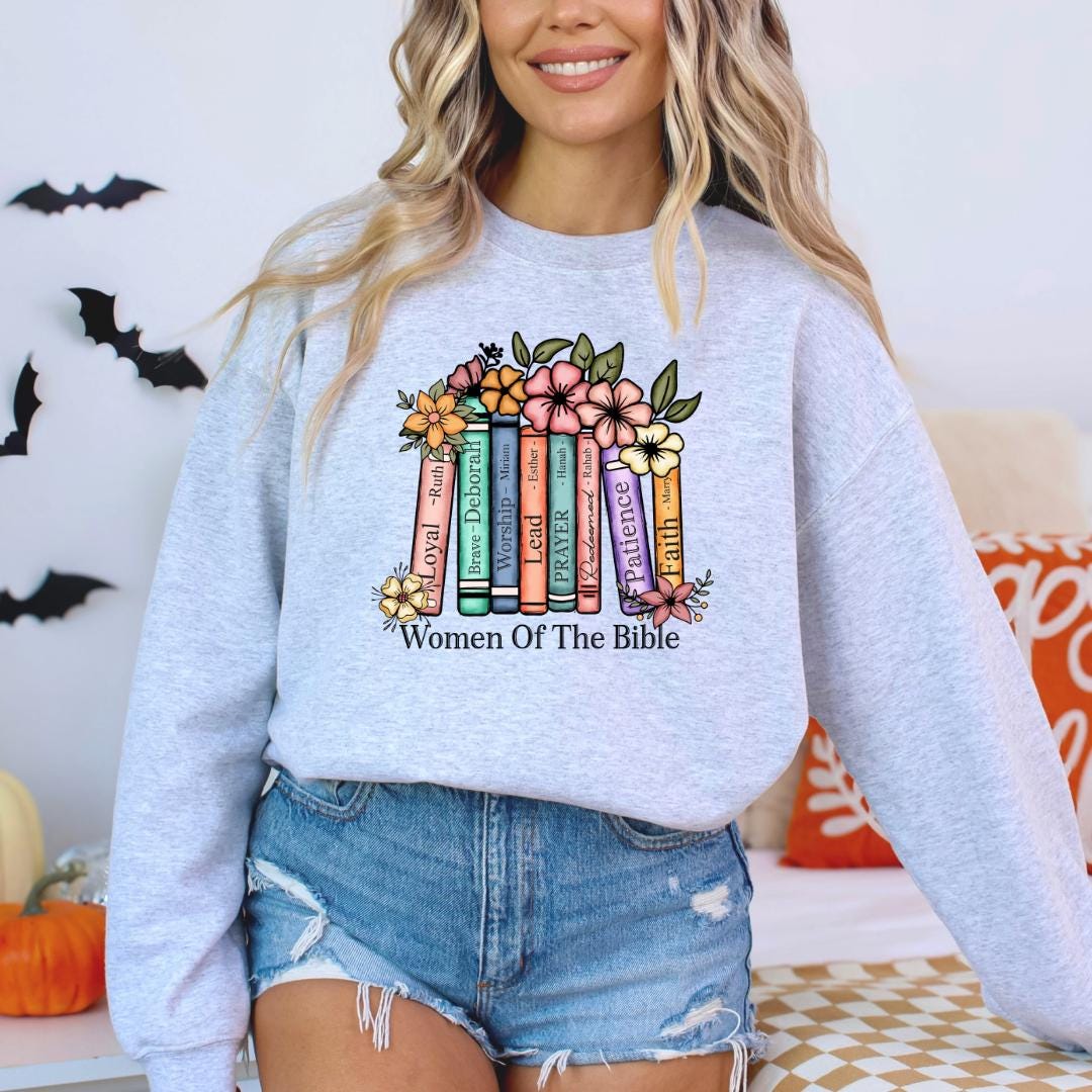 A woman wearing a gray sweatshirt with a colorful graphic design of books and flowers, along with the text "Women Of The Bible".
