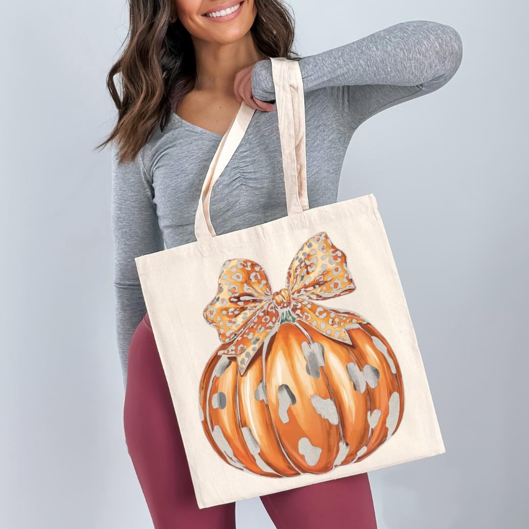 A woman is holding a white tote bag with a printed pumpkin design on it.