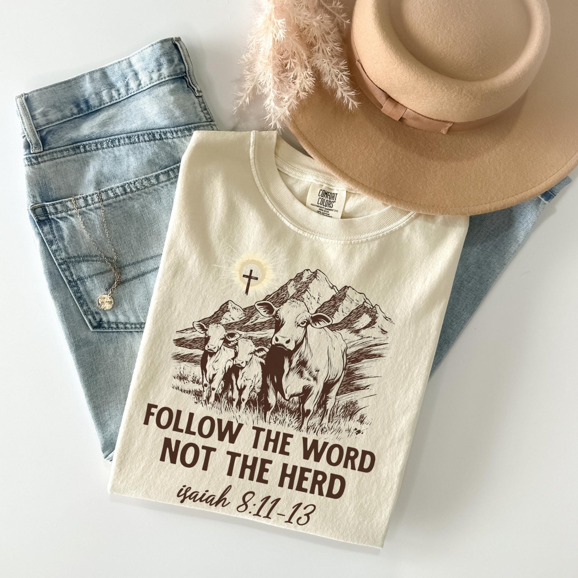 a white t-shirt with a graphic design, a pair of jeans, and a beige hat, all laid out on a white surface.