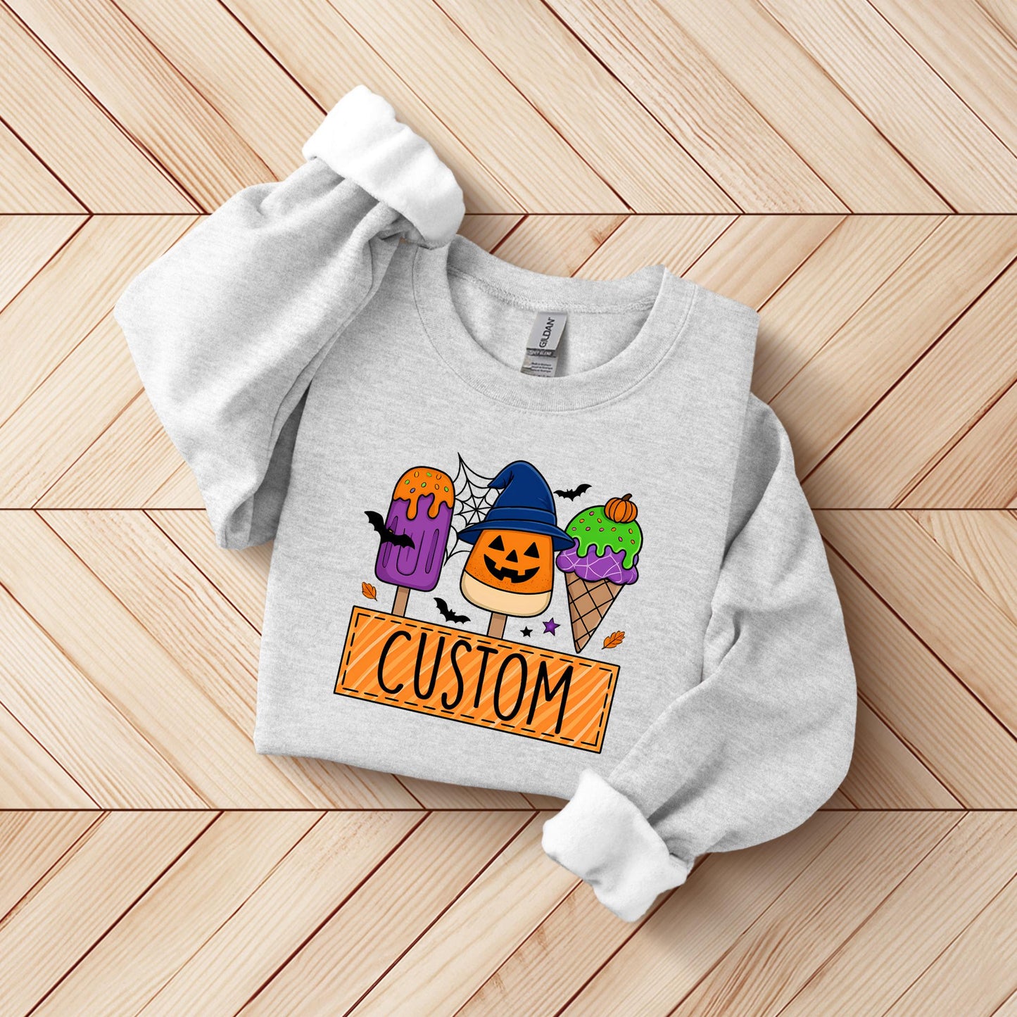 A gray sweatshirt with a Halloween-themed graphic design on it, featuring a pumpkin, bats, and a sign that says "CUSTOM".