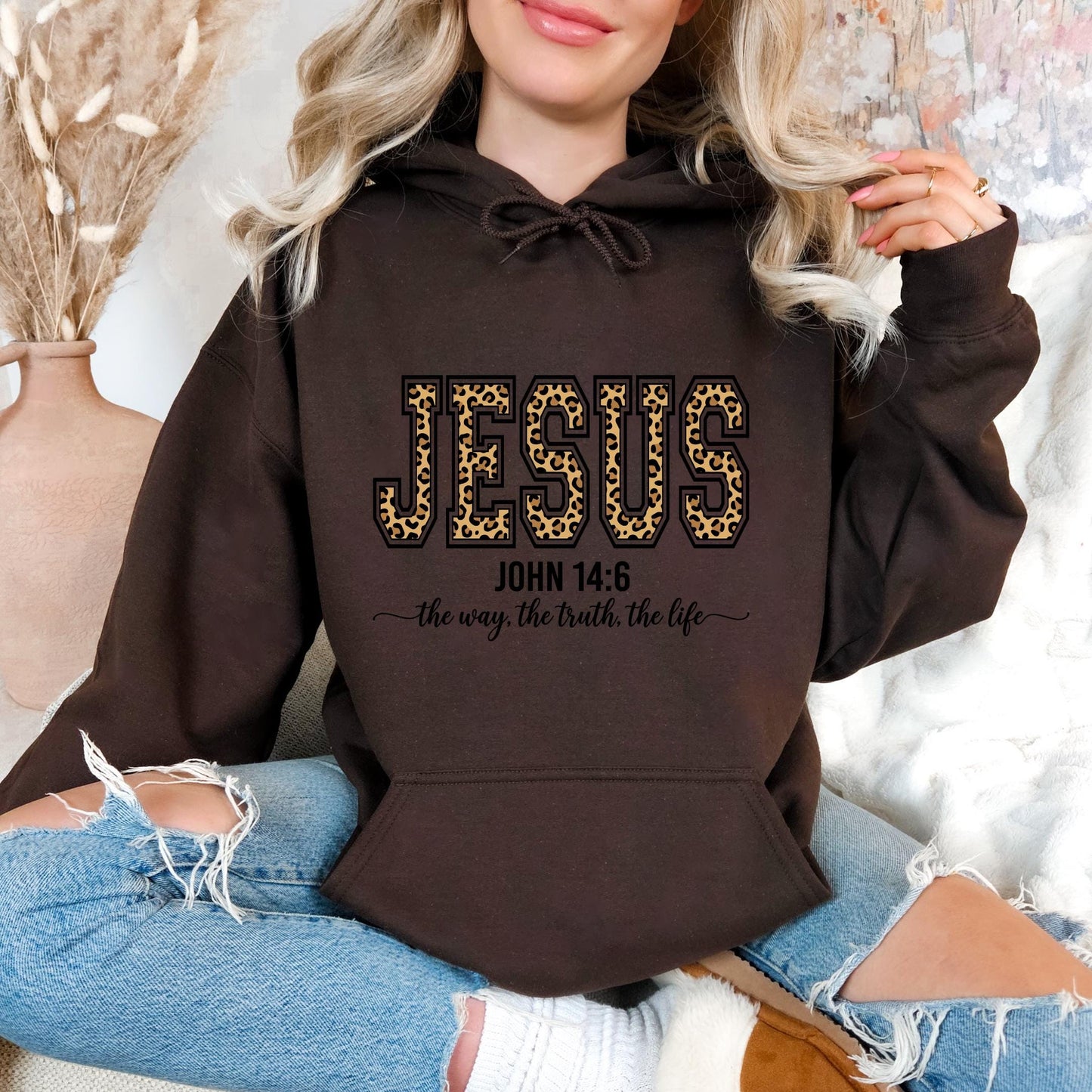 A woman wearing a brown hoodie with the text "JESUS" and "the way the truth, the life" printed on it.