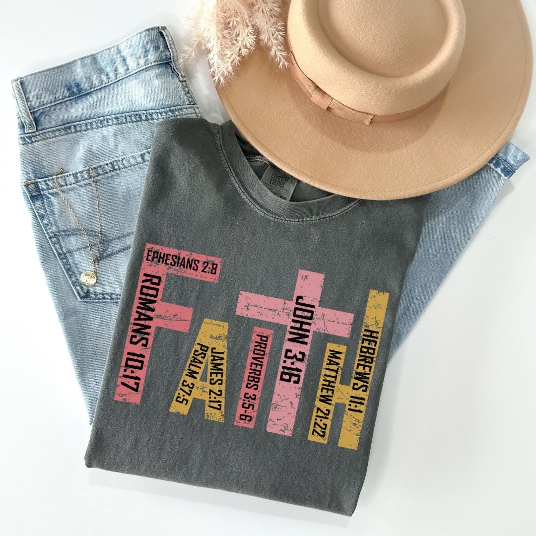 A gray t-shirt with text printed on it, along with a pair of jeans and a beige hat, all laid out on a white surface.