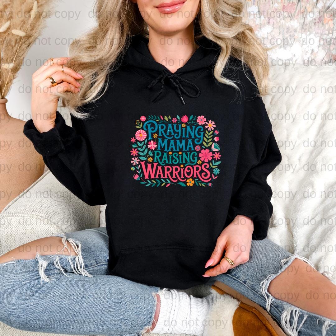 A woman wearing a black hoodie with a colorful graphic design and text, sitting on a couch.