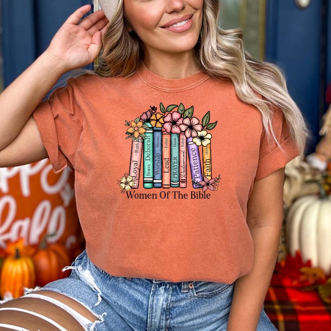 A woman wearing a t-shirt with a colorful graphic design of books and flowers, along with the text "Women Of The Bible".